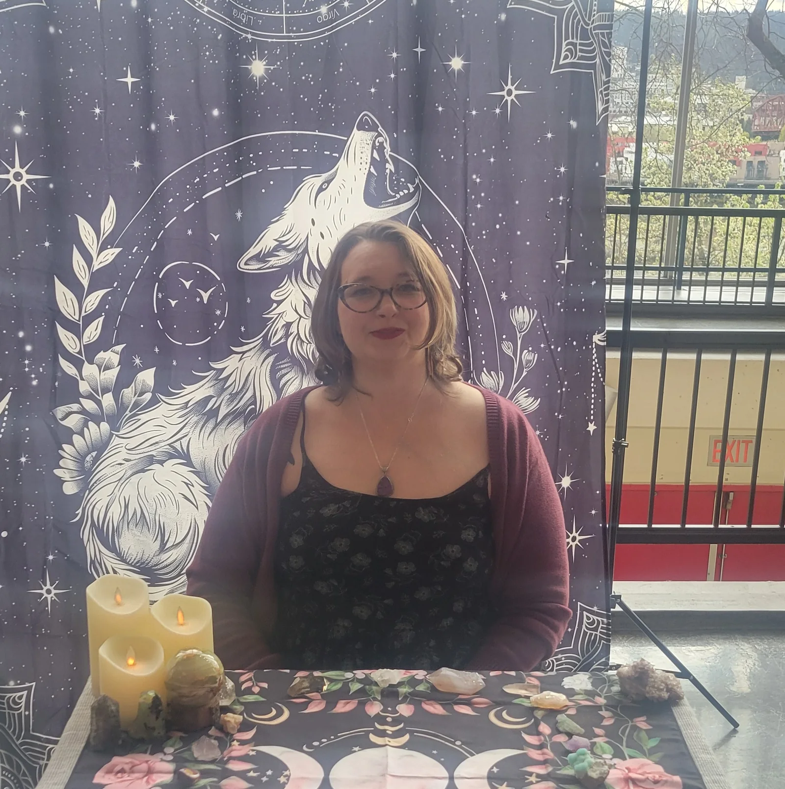 Crystal seated behind her tarot table with a wolf tapestry and candles.